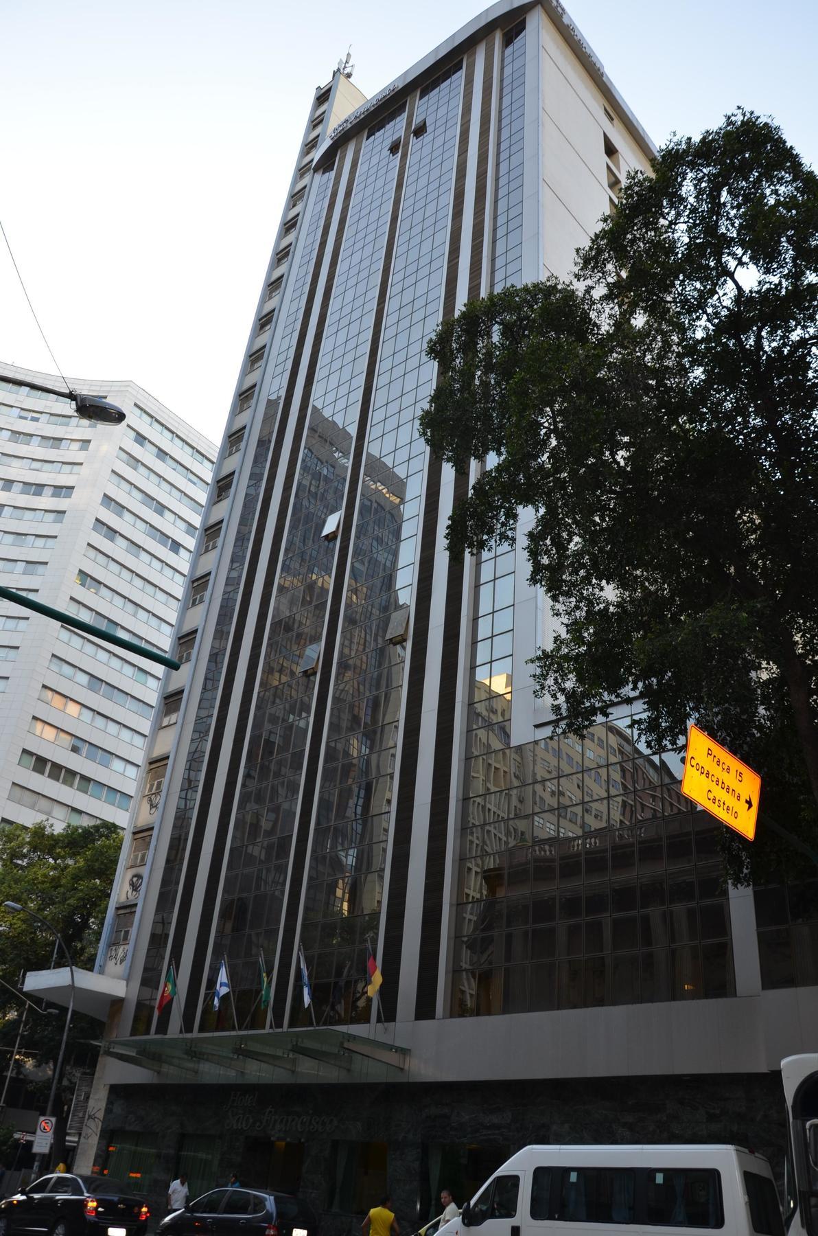 Hotel Atlantico Tower Rio de Janeiro Esterno foto The photo shows a city street with tall buildings. In the foreground, there is a modern glass skyscraper featuring reflective surfaces and vertical lines. Next to it, there's another building with a different architectural style, also made of glass. 